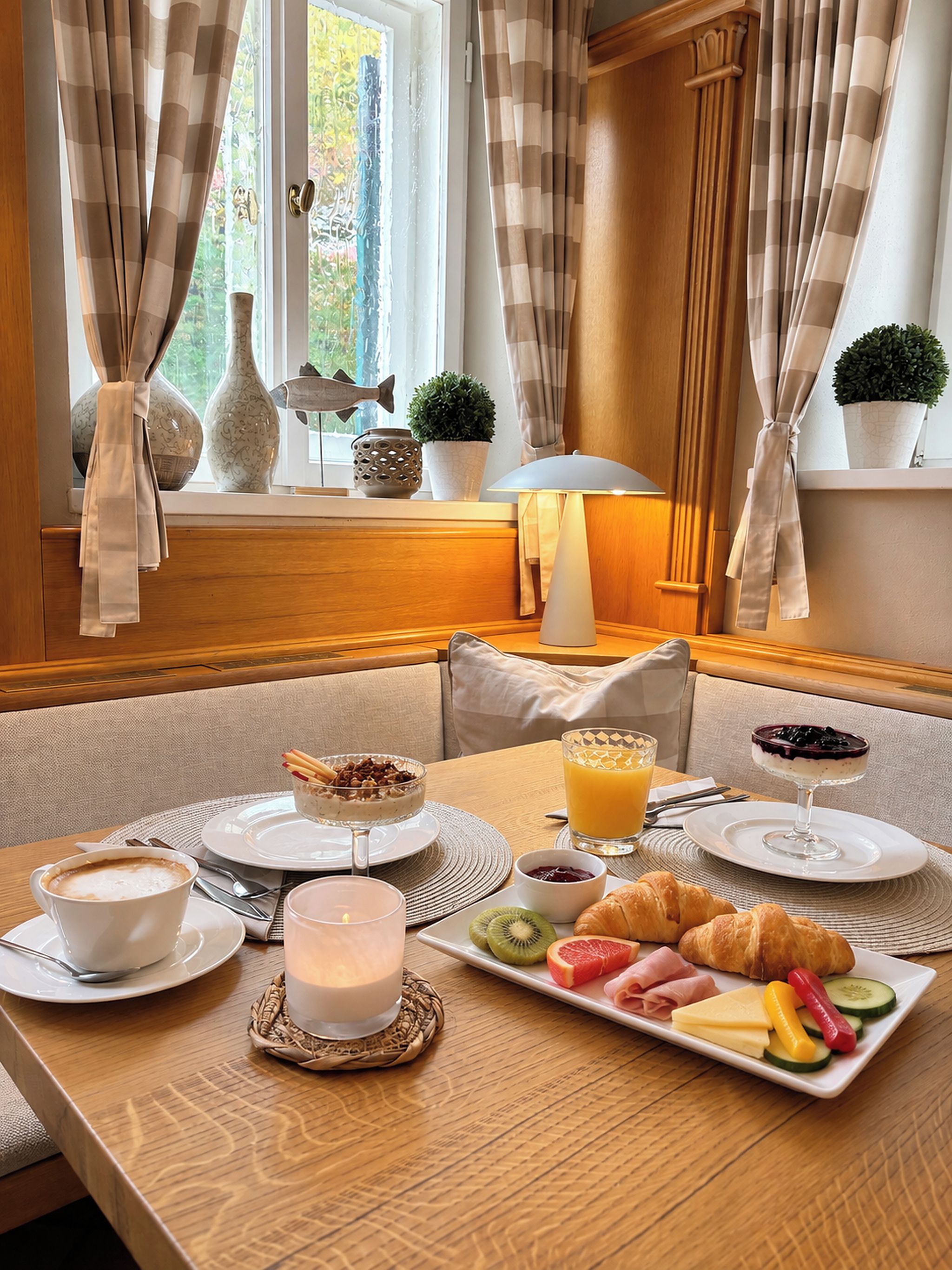 Une table mise pour le petit-déjeuner, avec une nappe pour deux personnes, comprenant des assiettes de nourriture, un verre de jus d’orange et une bougie.