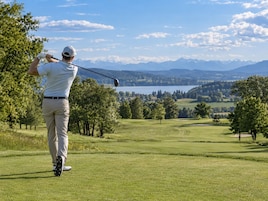 Un golfista en un campo de golf con vistas a montañas y un lago al fondo.