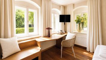 Een kamer met een houten bureau, een stoel, een bankje, een televisie en een raam met gordijnen.