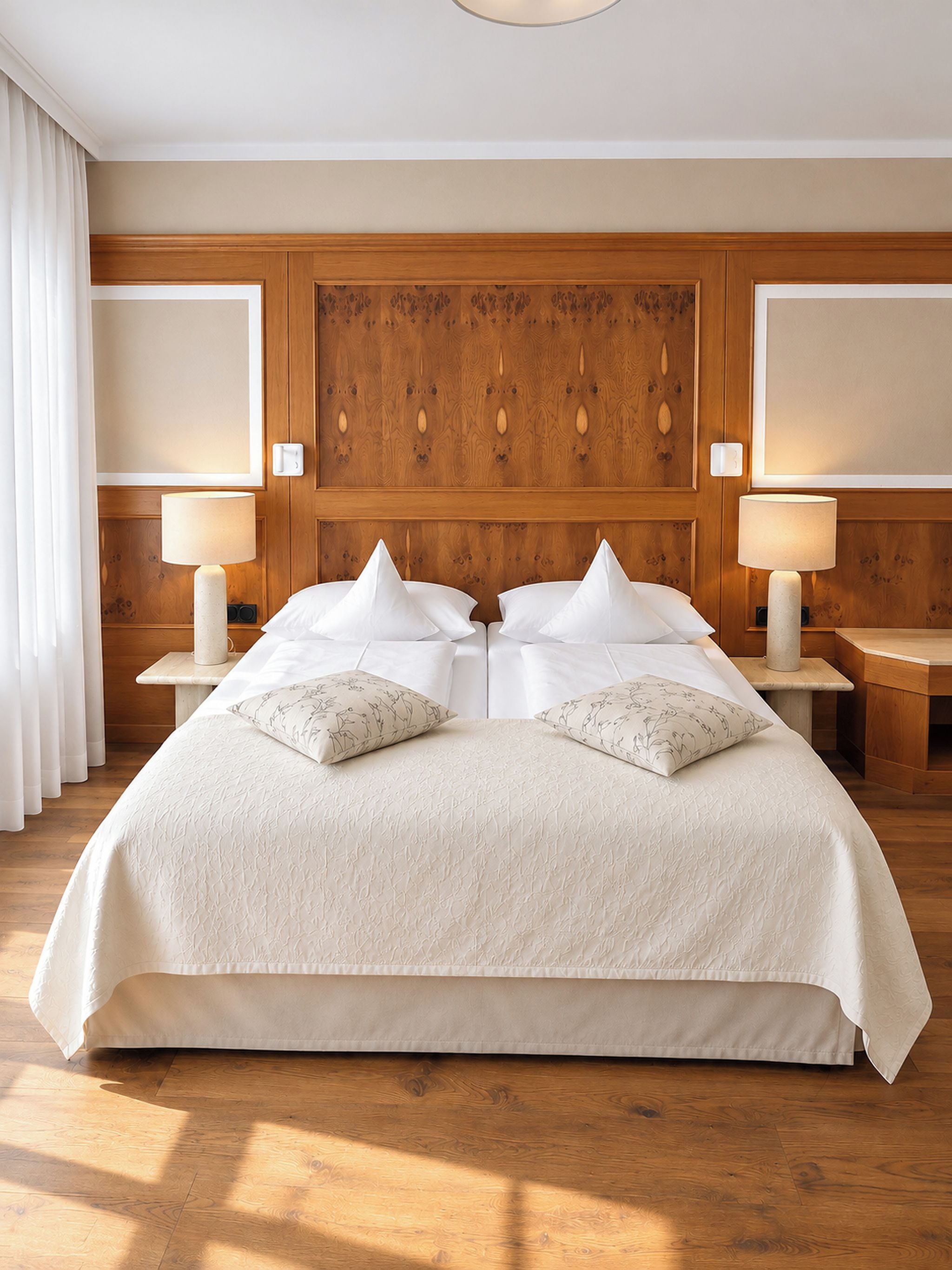 A large bed with a wooden headboard, two bedside tables with lamps, and a view of the room's wooden floor.