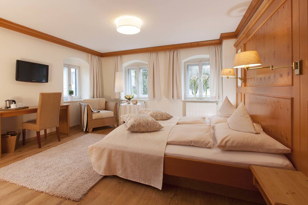 A bedroom with a bed, a desk, a chair, a TV, and a window with curtains.