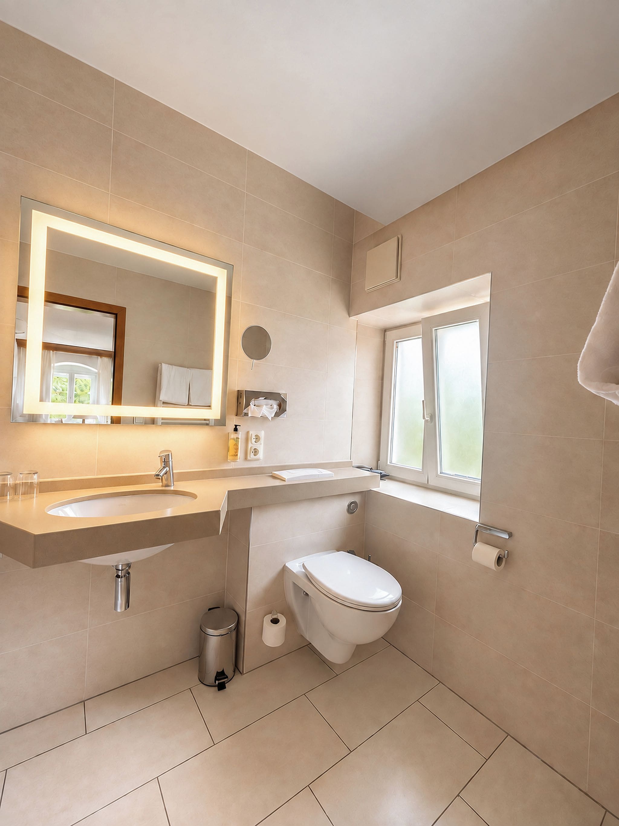Een moderne badkamer met een wastafel, spiegel, toilet en raam.