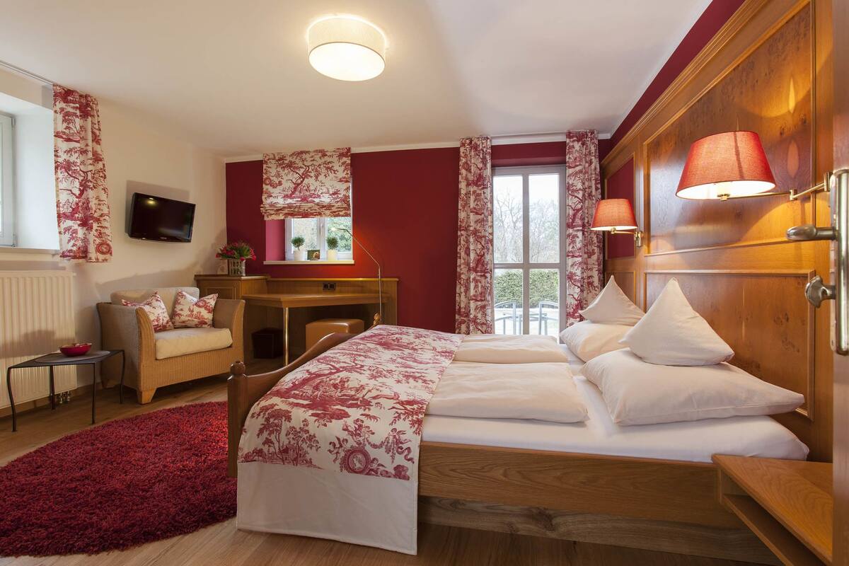 A hotel room with a bed, a desk, a chair, a TV, and a window with curtains.