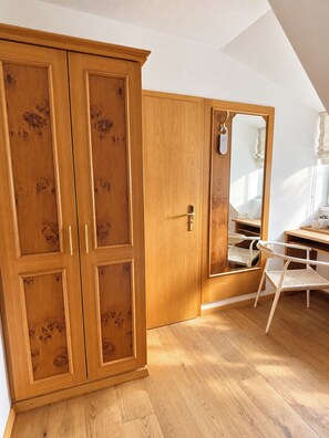 A room with a wooden wardrobe, a mirror, a chair, and a desk. - Hotel Fischerhaus (Starnberg)