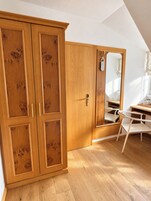 Quarto com guarda-roupa de madeira, espelho, cadeira e escrivaninha.