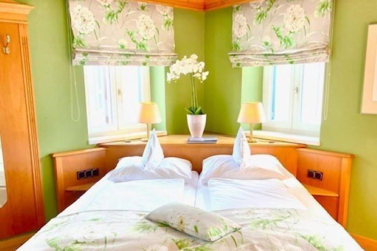 A bedroom with a large bed, two bedside tables, a window with a floral curtain, and a green wall.