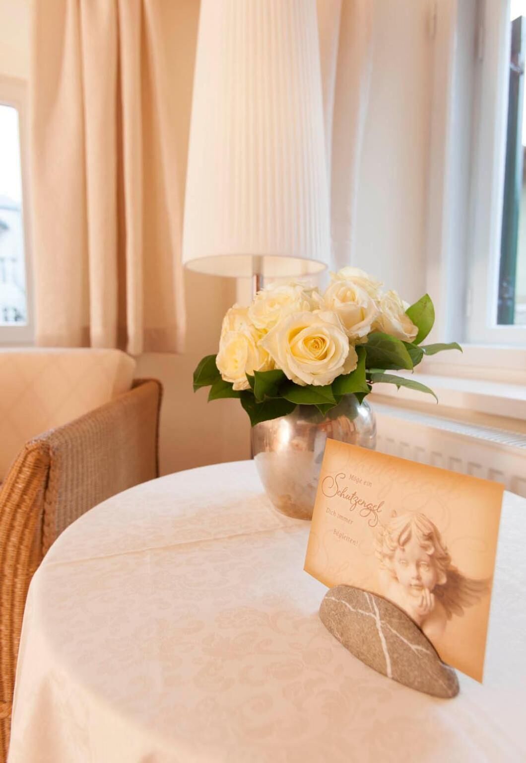 A round table with a white tablecloth, a vase of white roses, a framed picture, and a stone.