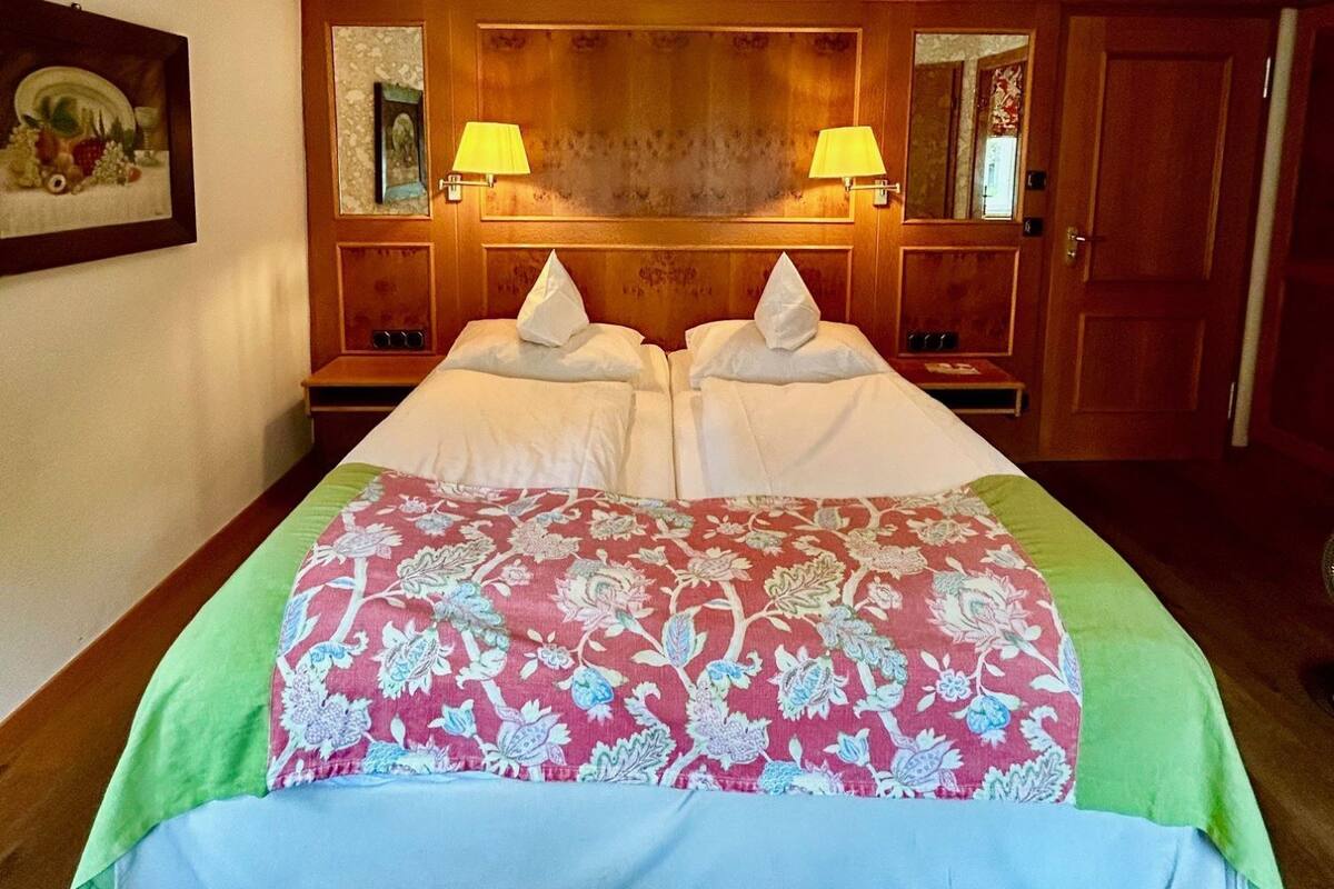 A double bed with a floral bedspread, two bedside lamps, a wooden headboard, and a mirror above the bed.