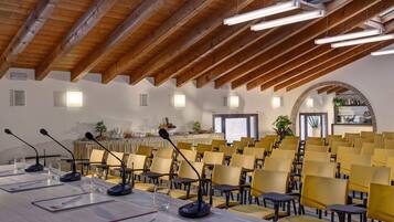 A conference room with a long table, multiple chairs, microphones, and a buffet area in the background.