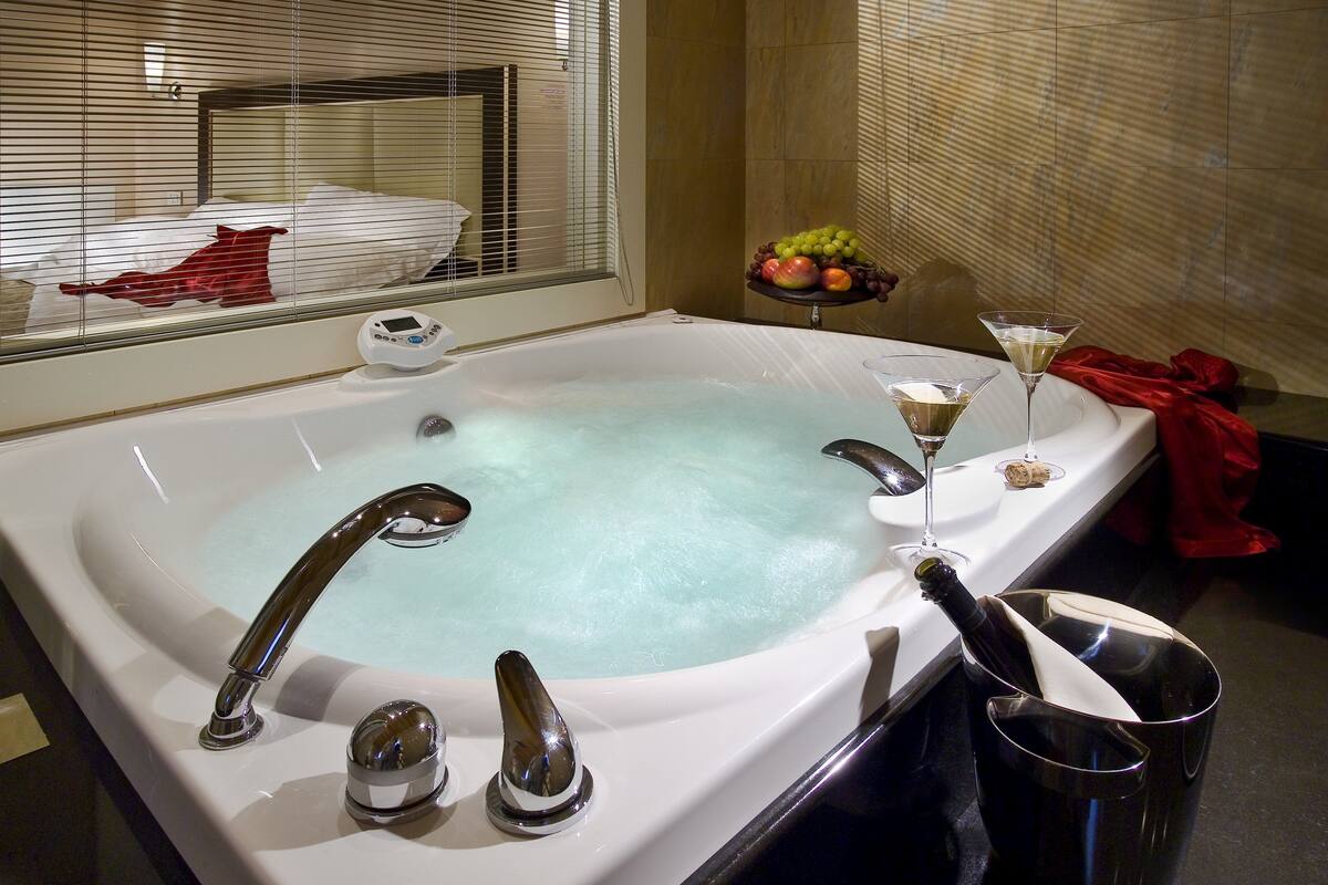 Una bañera grande y moderna con un panel de control, una copa de vino y un frutero al lado.