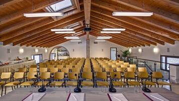 A conference room with rows of yellow chairs, a long table with microphones, and a high wooden ceiling with skylights.