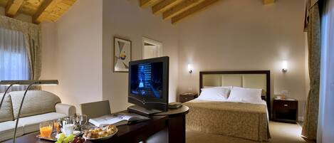 A hotel room with a wooden ceiling, a bed with a headboard, a desk with a laptop, a TV, and breakfast items.