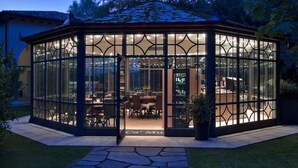 A glass-enclosed gazebo with a tiled roof, a central dining area with chairs, and a door labeled "Ca' Mura". - Ca' Mura' Hotel (Masera di Padova)