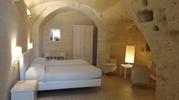 A bedroom with a large arched stone ceiling, a double bed, a small bedside table, a chair, and a mirror on the wall.