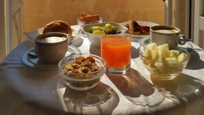 Una mesa de desayuno con diversos alimentos y un vaso de jugo de naranja, con vista a un acantilado rocoso y edificios.
