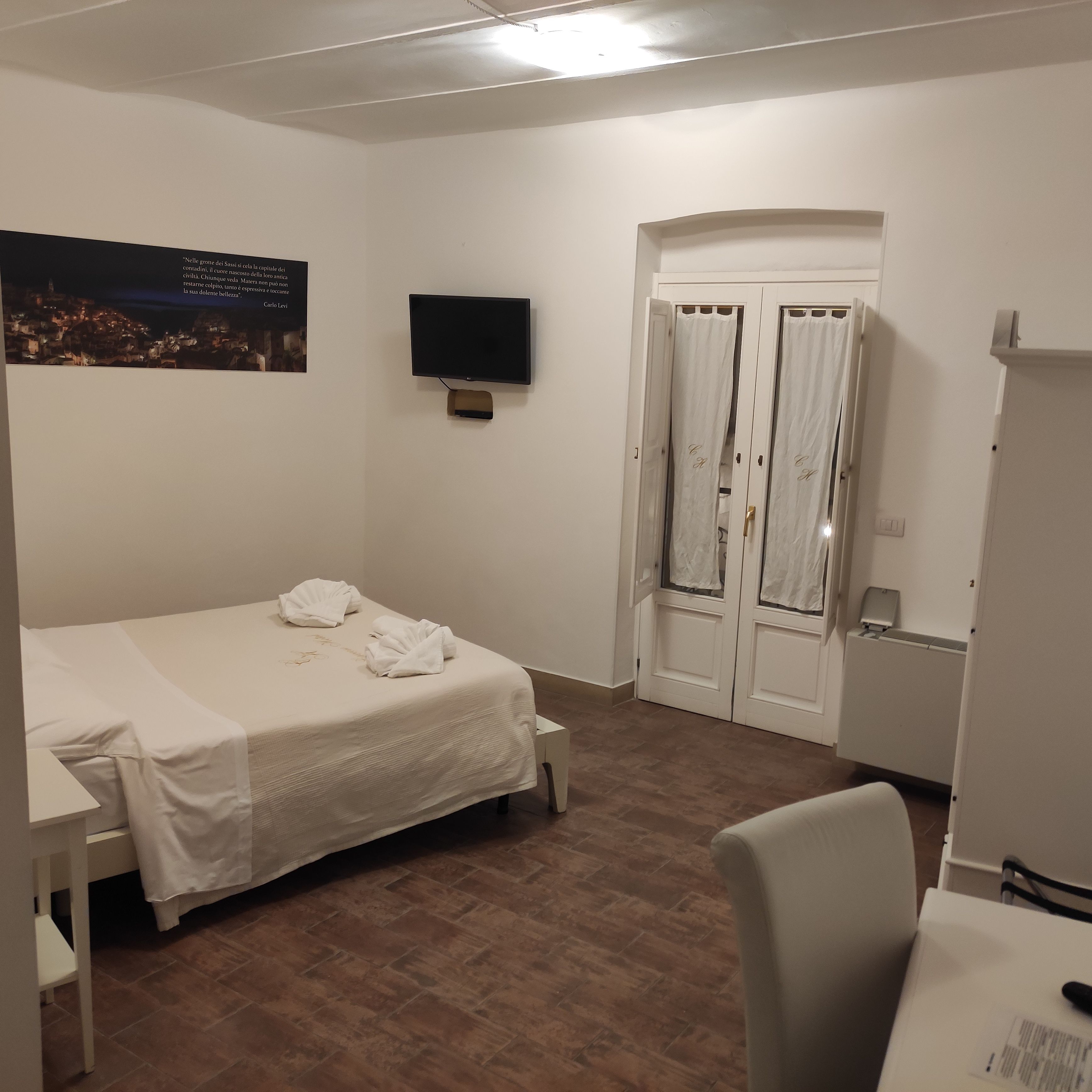 A hotel room with a bed, a desk, a television, and a door with curtains.