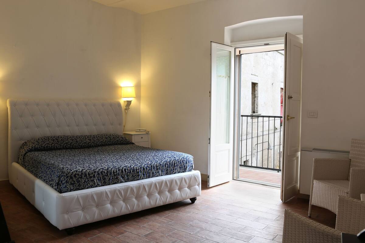 A bedroom with a bed, bedside lamp, and an open door to a balcony.