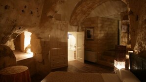 Una habitación con paredes de piedra, un armario de madera, una cama y un ventanal que deja entrar luz natural.
