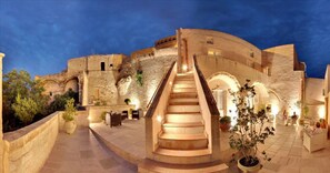 A stone staircase leading to a building with arches, surrounded by outdoor seating and potted plants. - Caveoso Hotel (Matera)