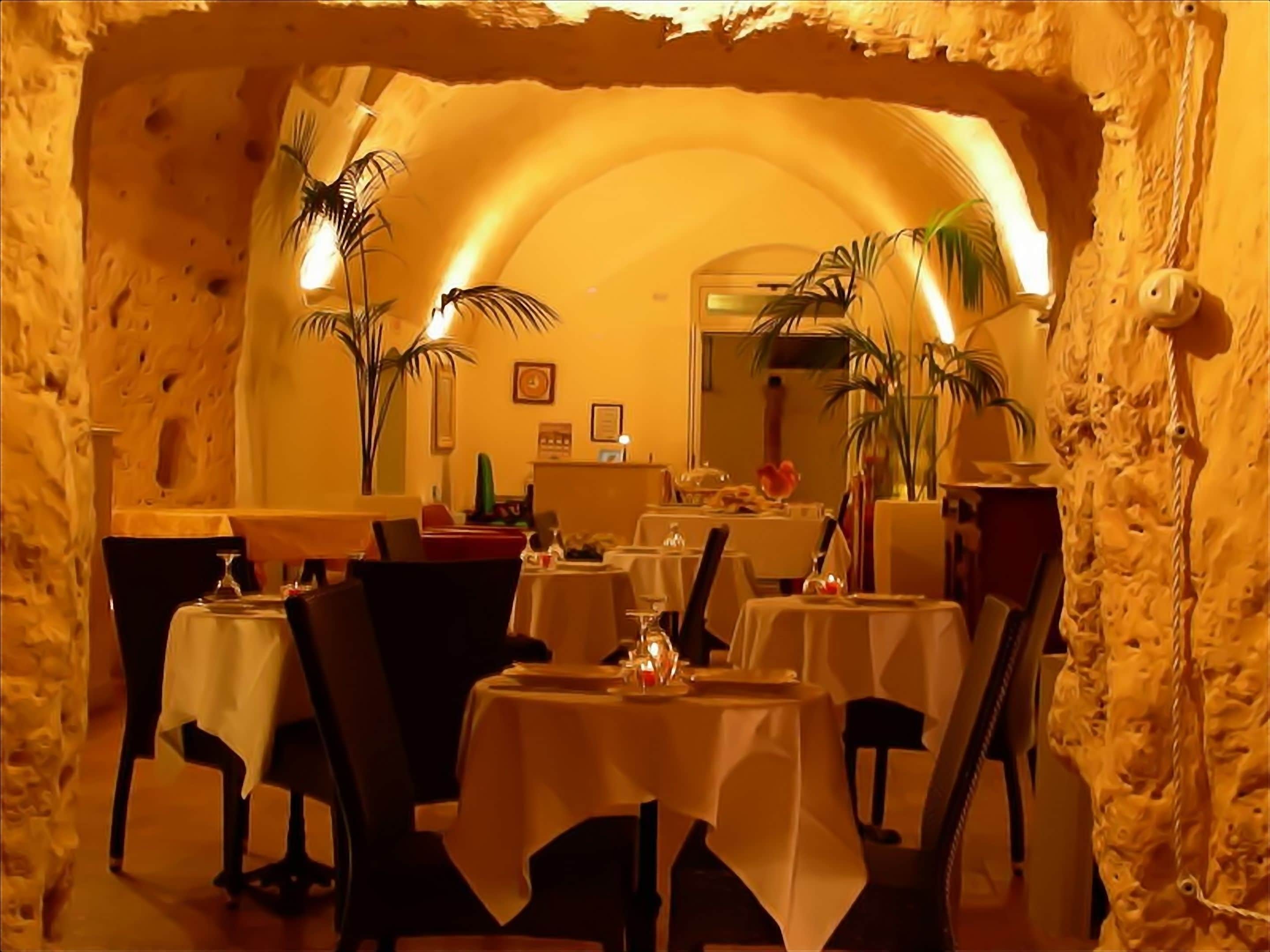An interior with tables and chairs, a stone wall, and potted plants.