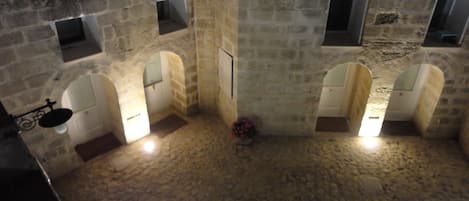 A stone-walled courtyard with arched doorways and a central column, suggesting a historical or traditional setting.