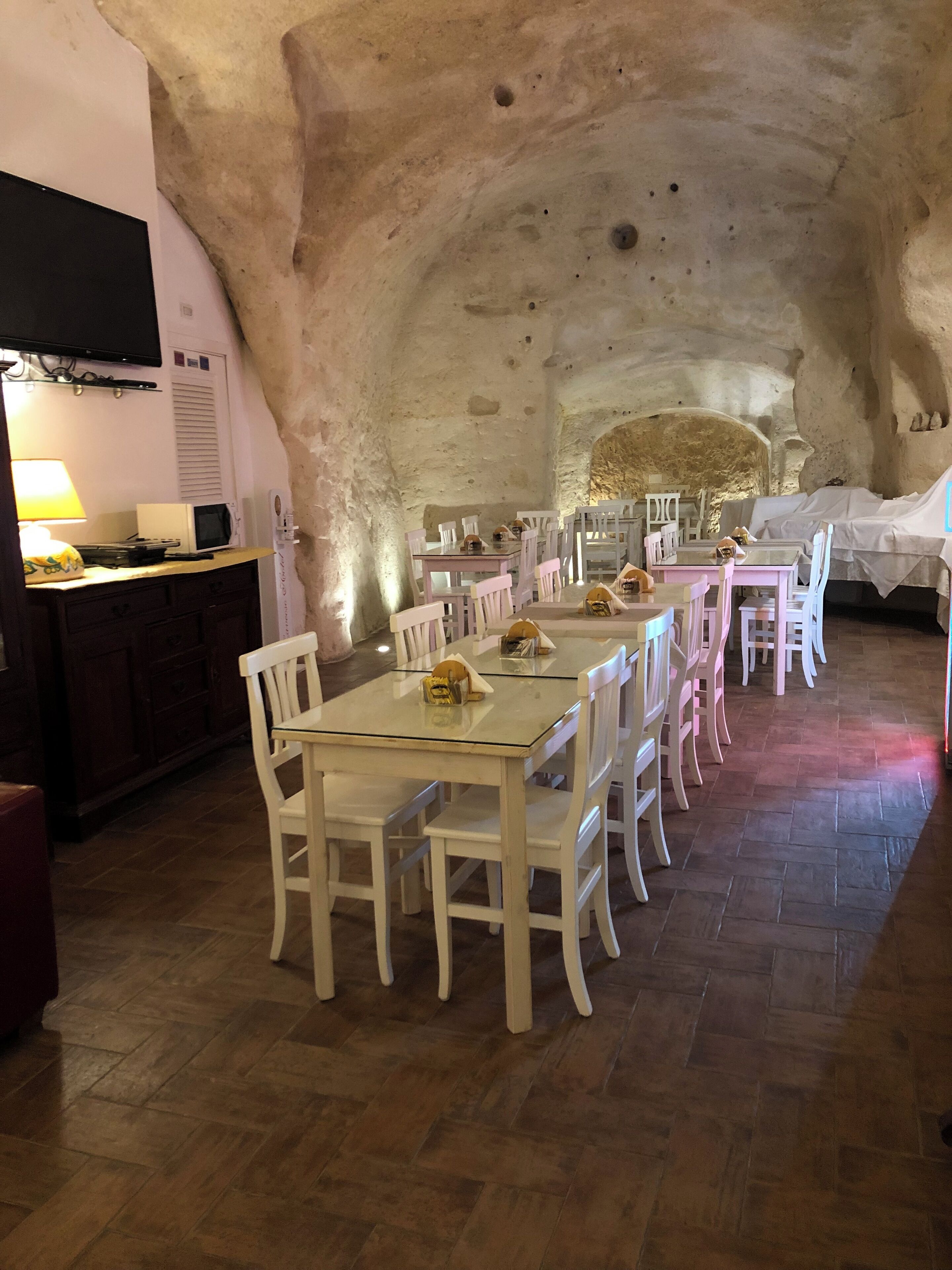 A dining area with white chairs and tables, a wooden floor, and a stone wall.