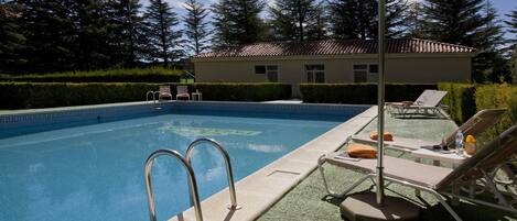 Ein Swimmingpool mit gefliestem Deck, Liegestühlen und einer Pergola, die Schatten spendet.