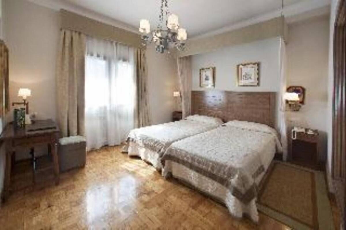 Un dormitorio con dos camas, un aparador de madera, una mesita de noche, una araña y una ventana con cortinas.