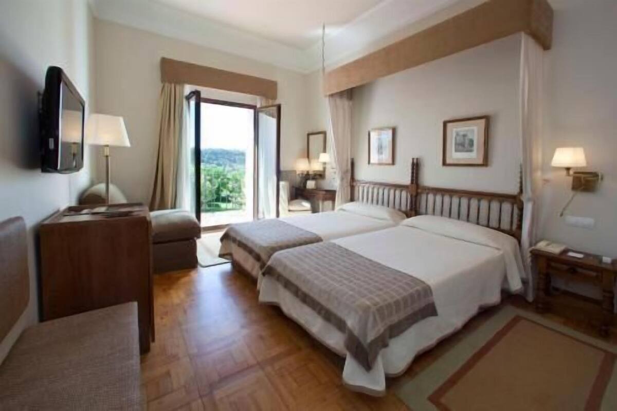 Habitación de hotel con dos camas, un escritorio, una silla, un televisor y una ventana con vistas.