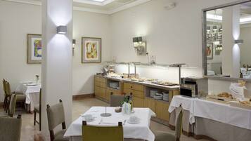 A dining area with tables set for breakfast, a buffet counter with various food items, and a large mirror reflecting the room.