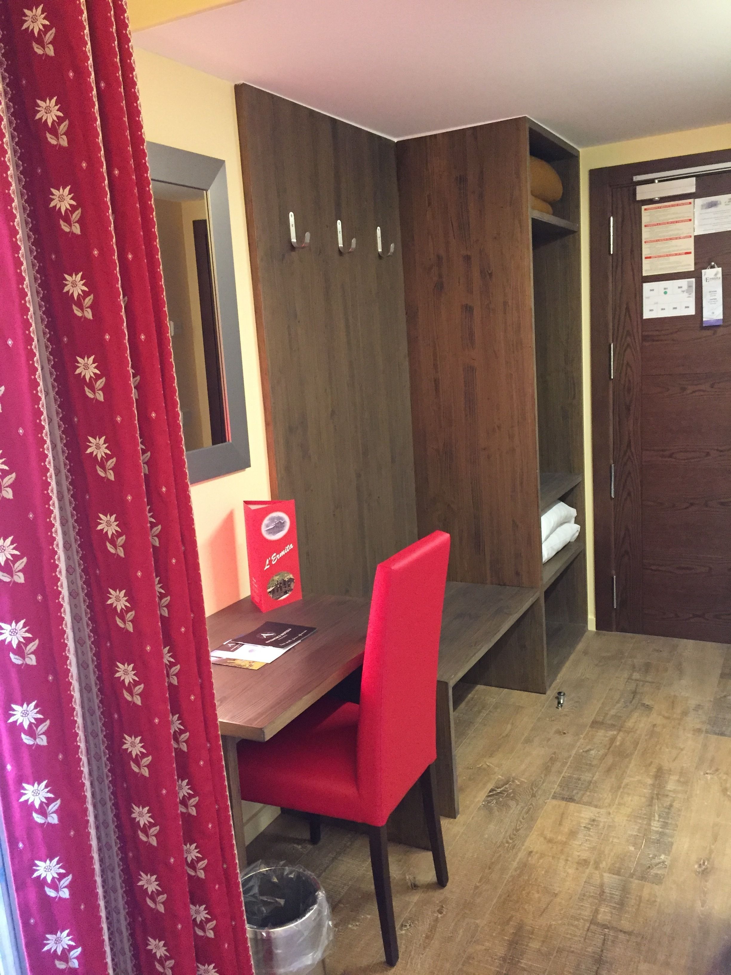 Habitación de esquina con armario de madera, una silla roja y una mesita pequeña.