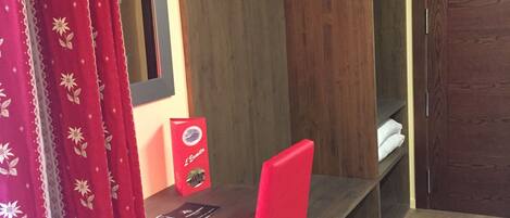 Habitación de esquina con armario de madera, una silla roja y una mesita pequeña.