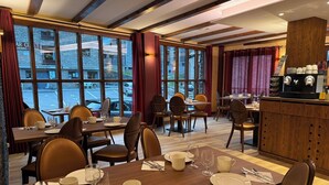 A restaurant with wooden tables and chairs, large windows, and a bar area.