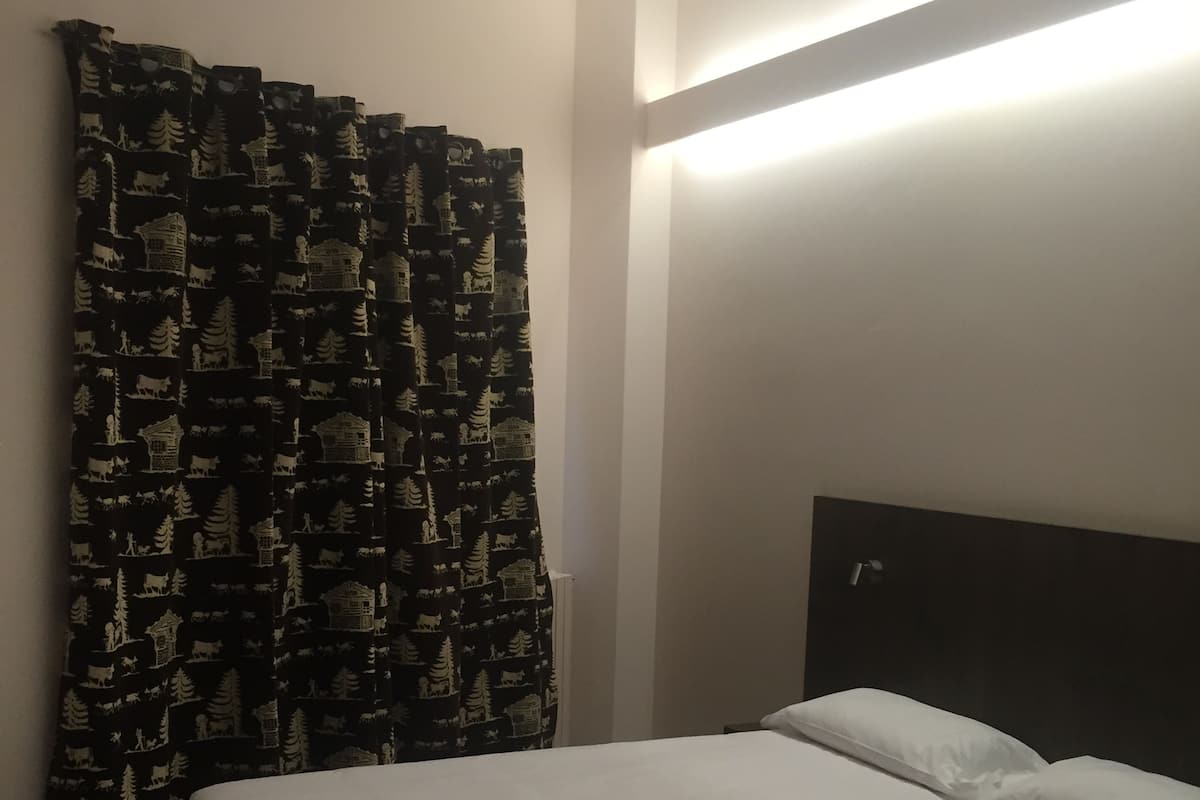 A hotel room with a bed, a headboard, and a curtain with a forest pattern.