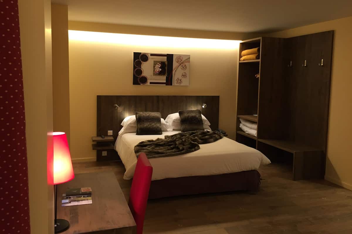 A hotel room with a bed, bedside table, lamp, and a wardrobe.