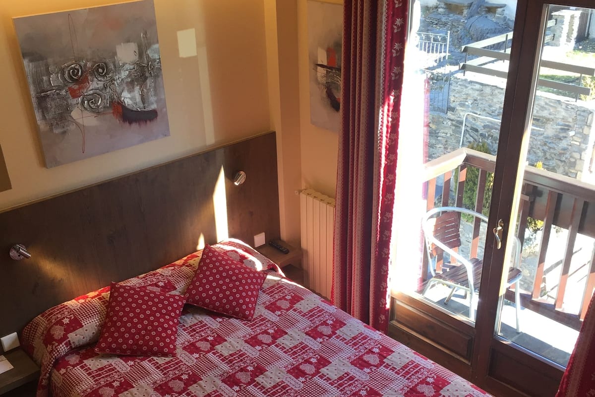 A bedroom with a bed, a headboard, a painting, a window with curtains, and a view of the outside.