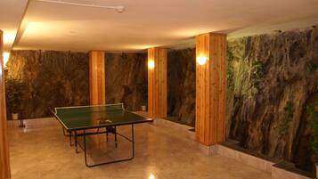 Una mesa de ping pong en una habitación con un mural de pared de roca y pilares de madera.