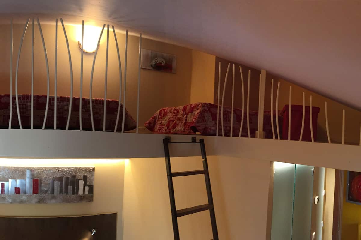 A room with a bunk bed, a ladder, a wall-mounted shelf with books, and a radiator.