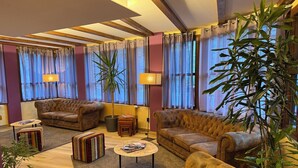 A spacious living room with two sofas, a coffee table, and a striped ottoman. There are potted plants and a lamp.