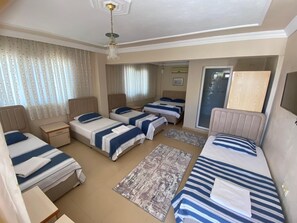 Een hotelkamer met drie bedden, een bureau, een stoel, een plafondventilator en een schuifdeur van glas.