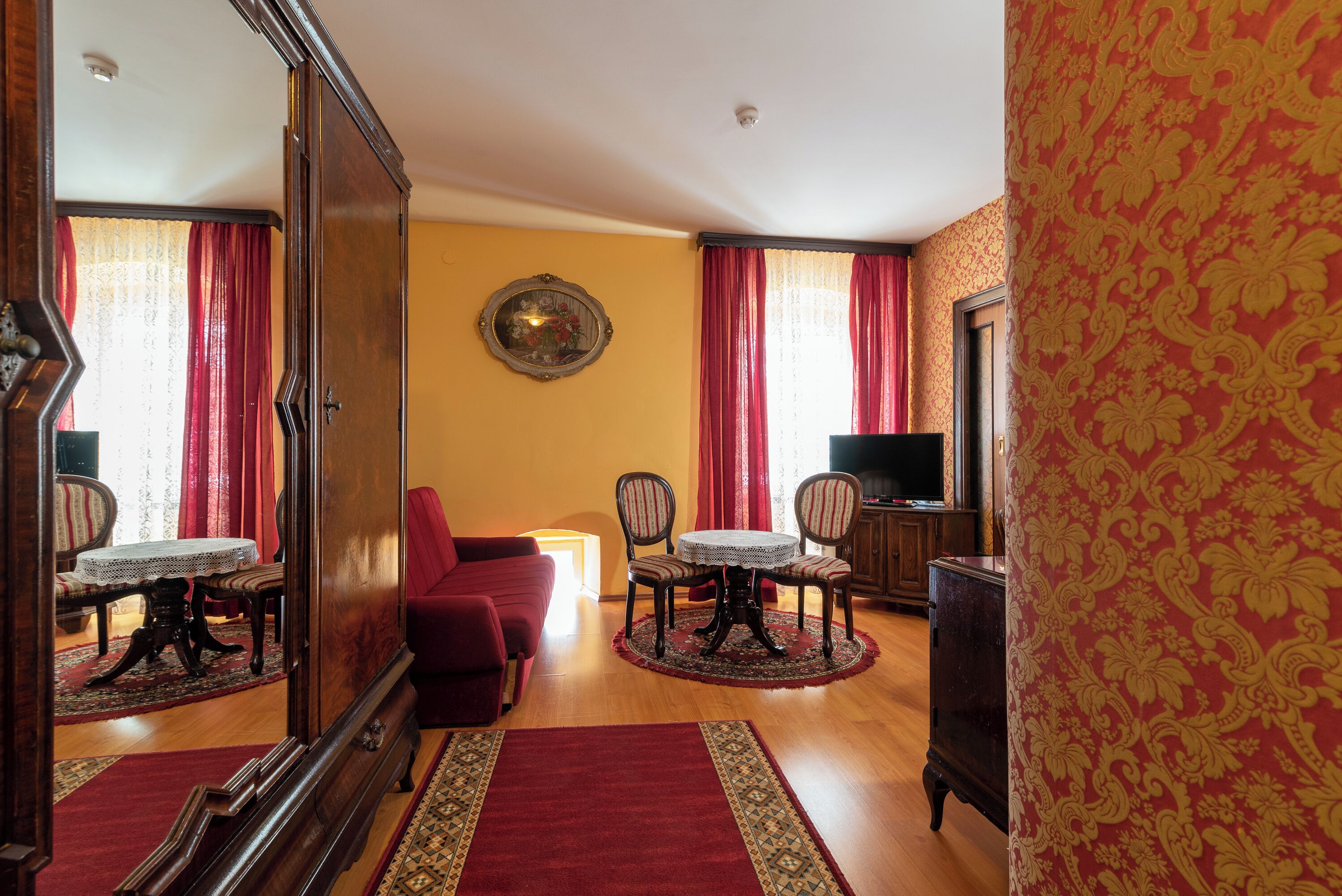 A room with a wooden floor, a red sofa, a dining table with chairs, a TV, and a mirror.