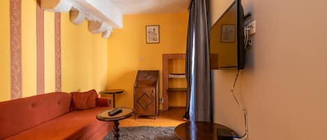 Una habitación acogedora con un sofá rojo, un mueble de madera pequeño, una mesa redonda y una cortina colgada.