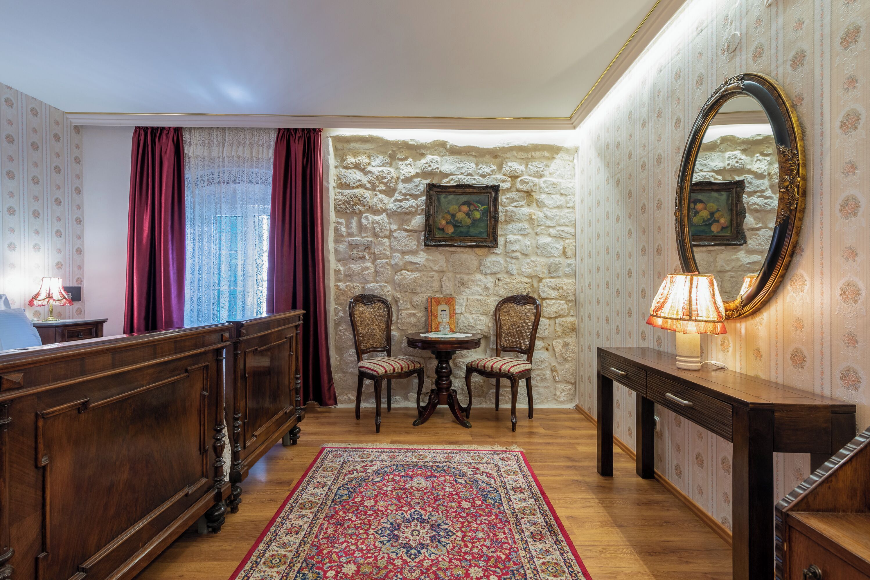 A room with a wooden bed, a small round table with chairs, a lamp, and a mirror on a dresser.