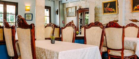 A dining area with ornate wooden chairs and tables, stone walls, and framed artwork.