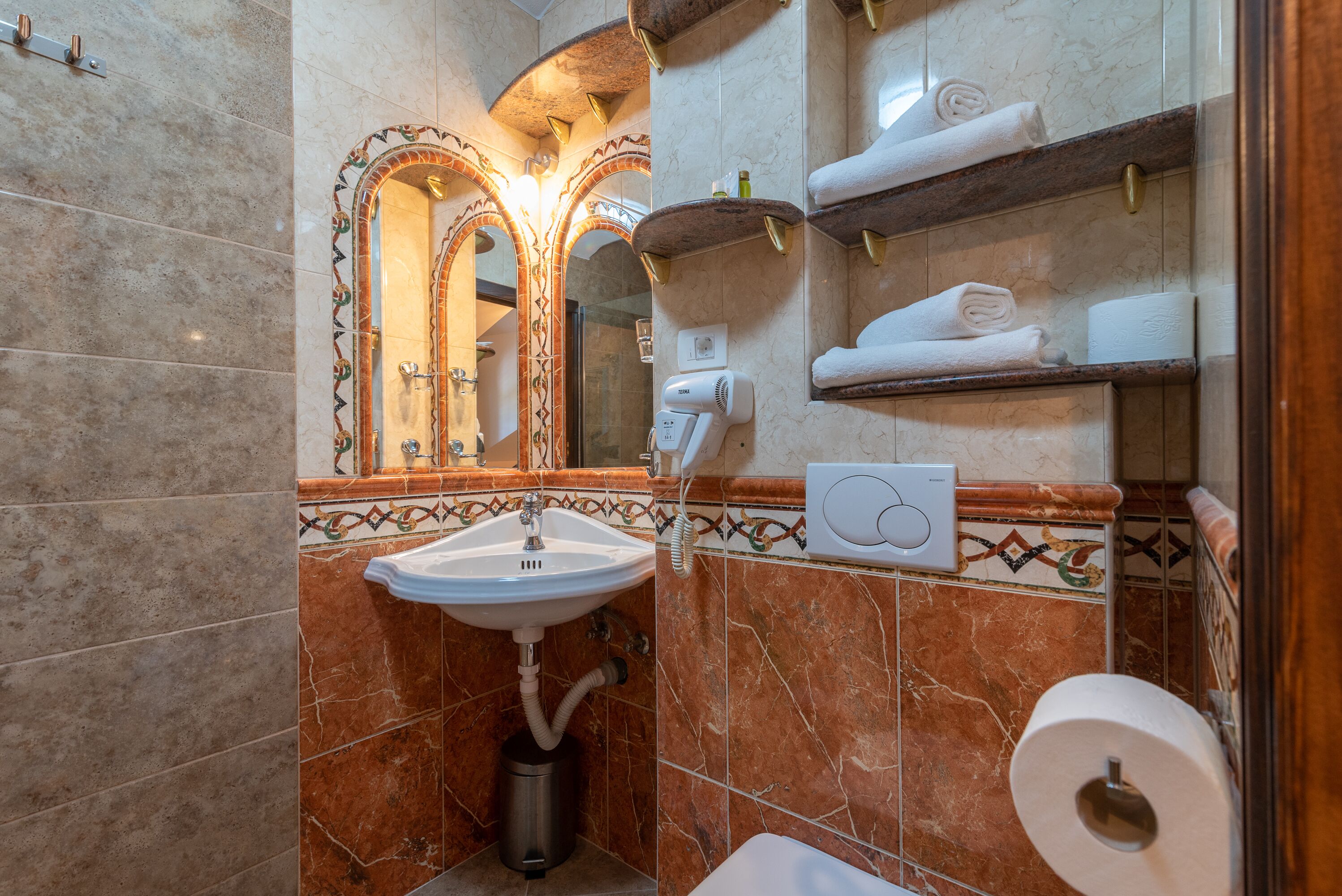 A bathroom with a sink, mirror, towel racks, and a toilet.