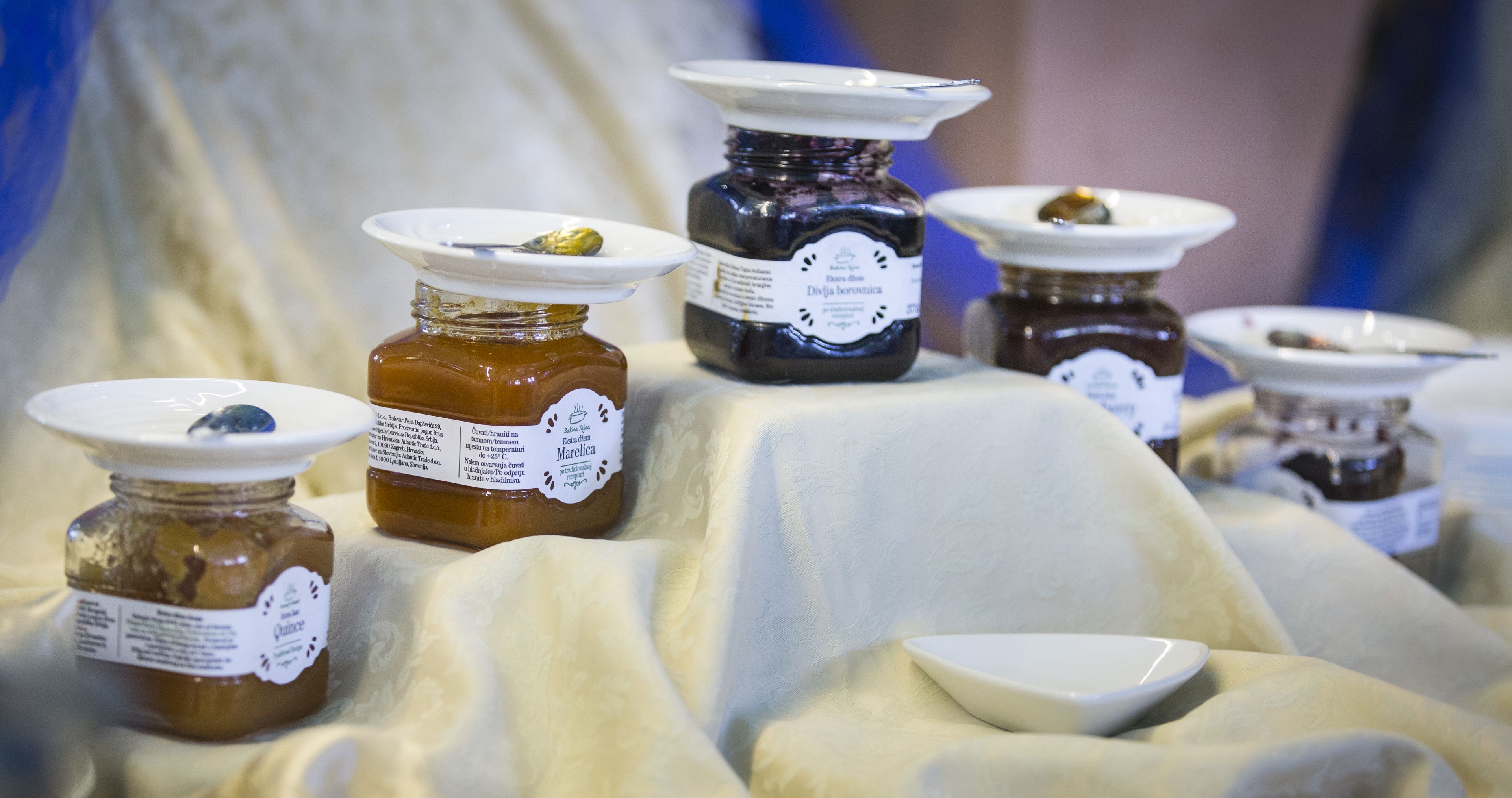 A display of various jars of preserves on a table with a white cloth.