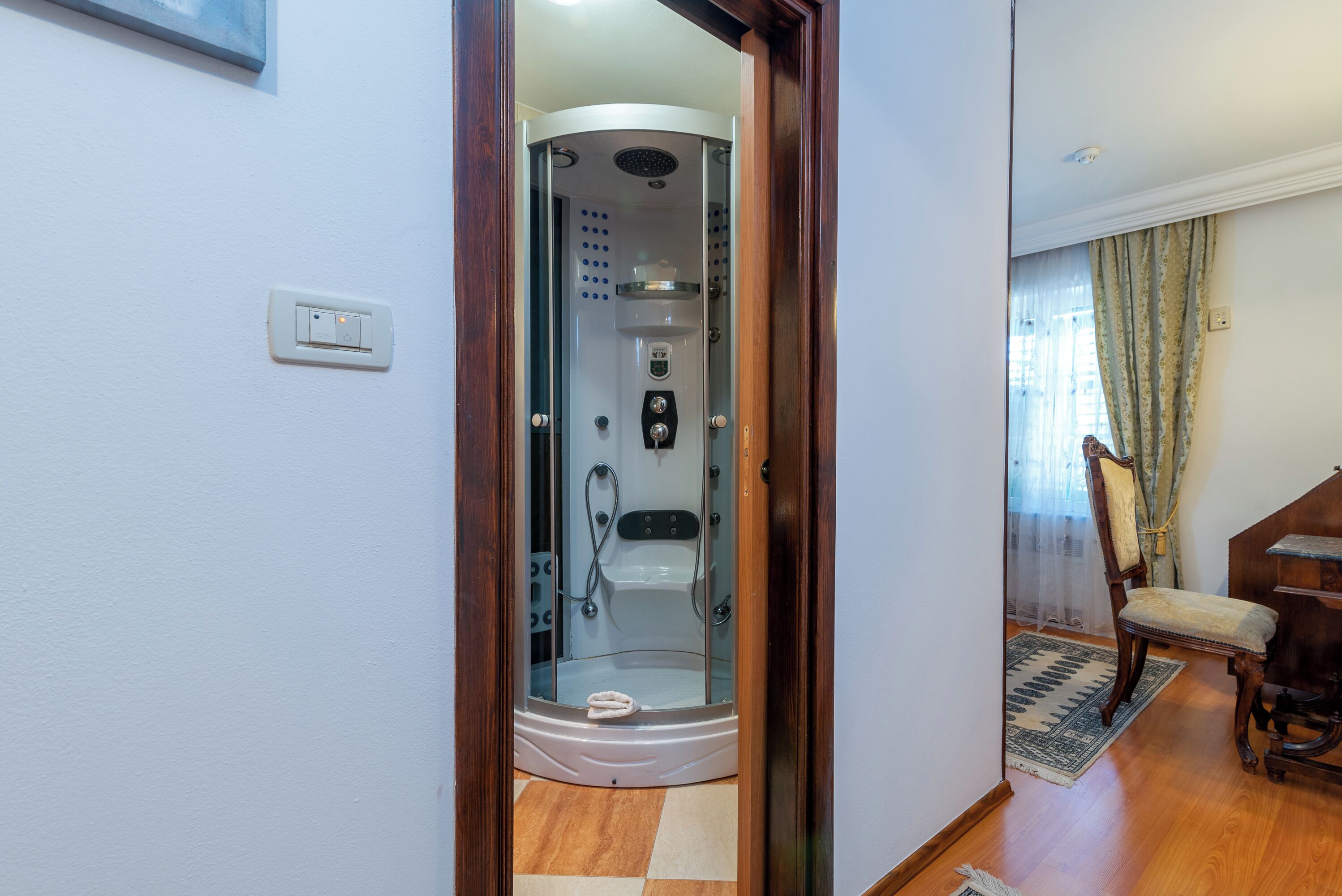 Une salle de bain moderne dotée d’une douche à parois de verre, d’un panneau de commande visible et d’un plancher en bois.