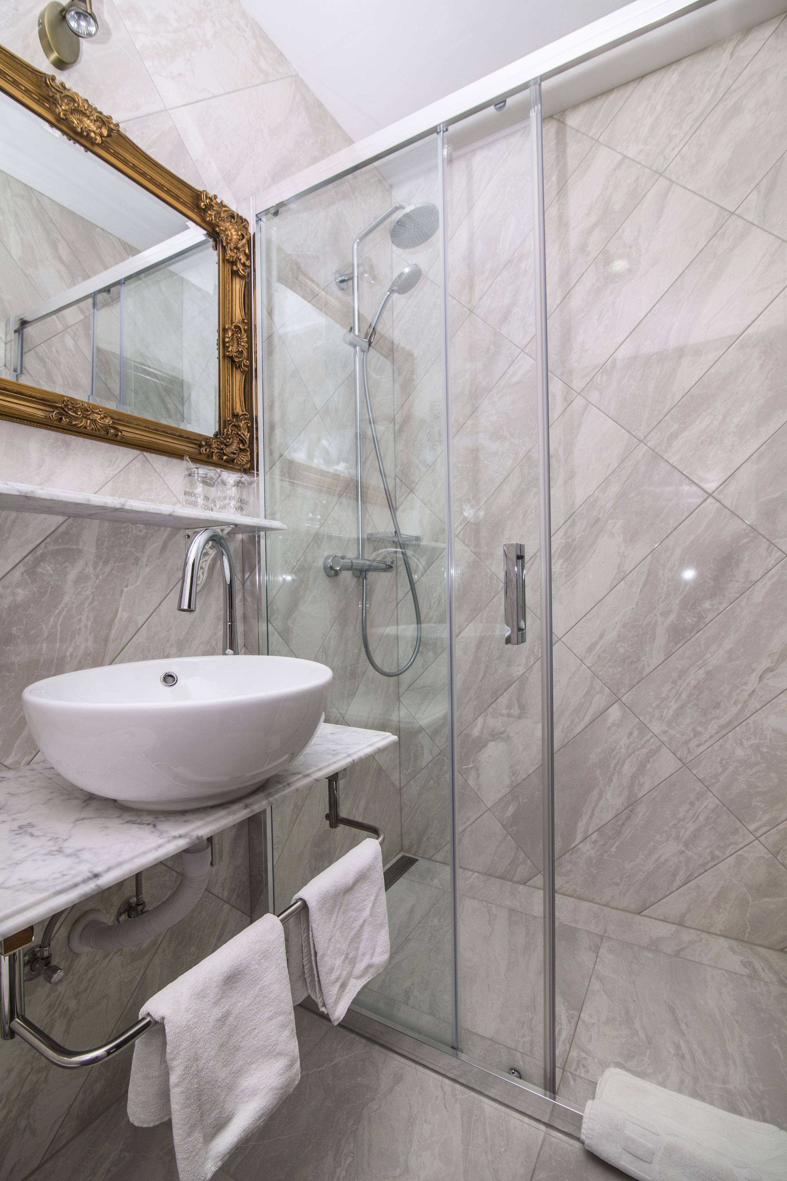 A modern bathroom with a white sink, a glass shower enclosure, and a marble-tiled shower area.