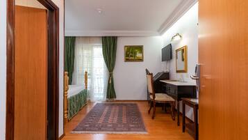 Una habitación con piso de madera, una cama con cortinas verdes, un escritorio con una silla y un cuadro en la pared.