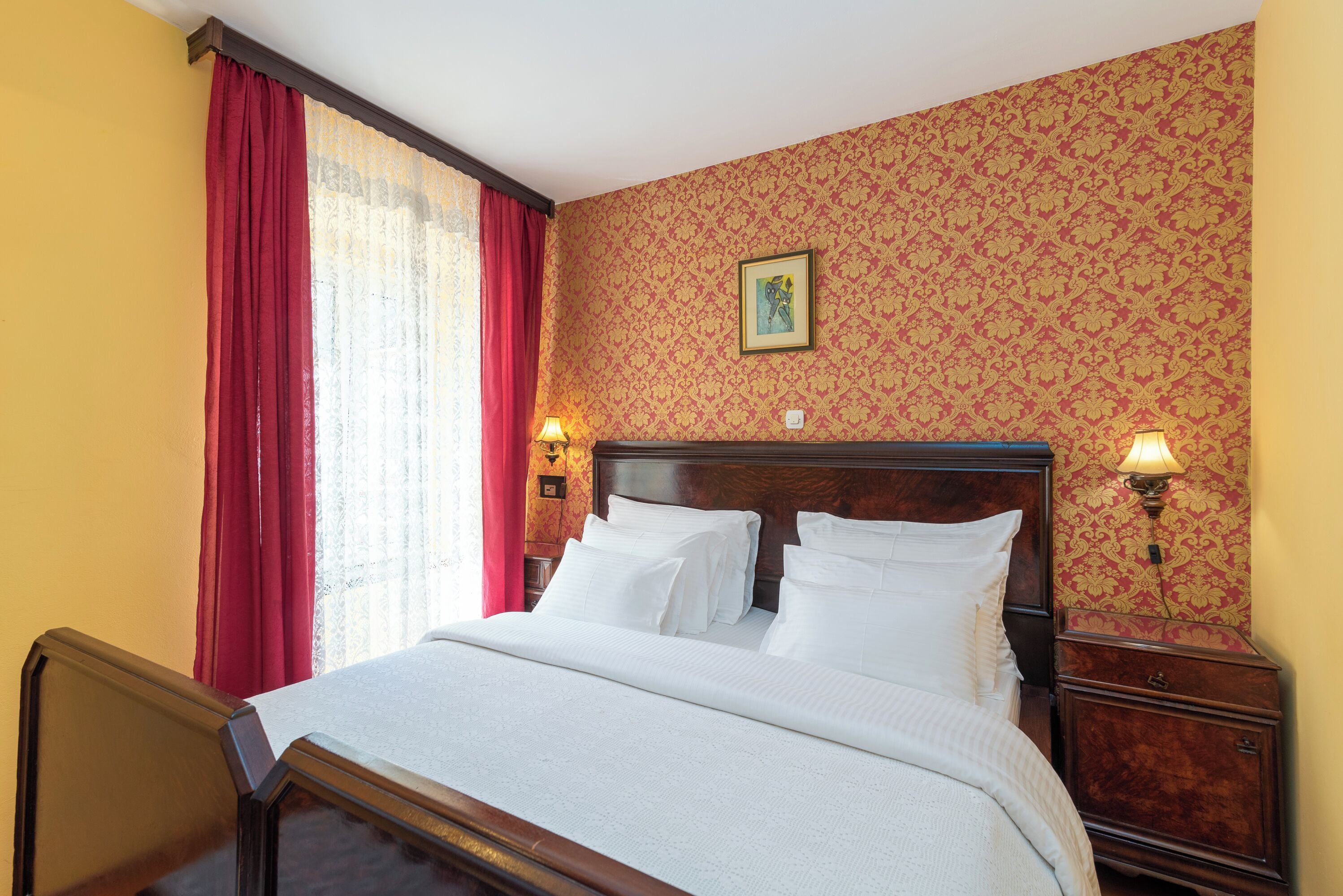 Una cama bien hecha con sábanas blancas, cabecera de madera y dos lámparas de noche.